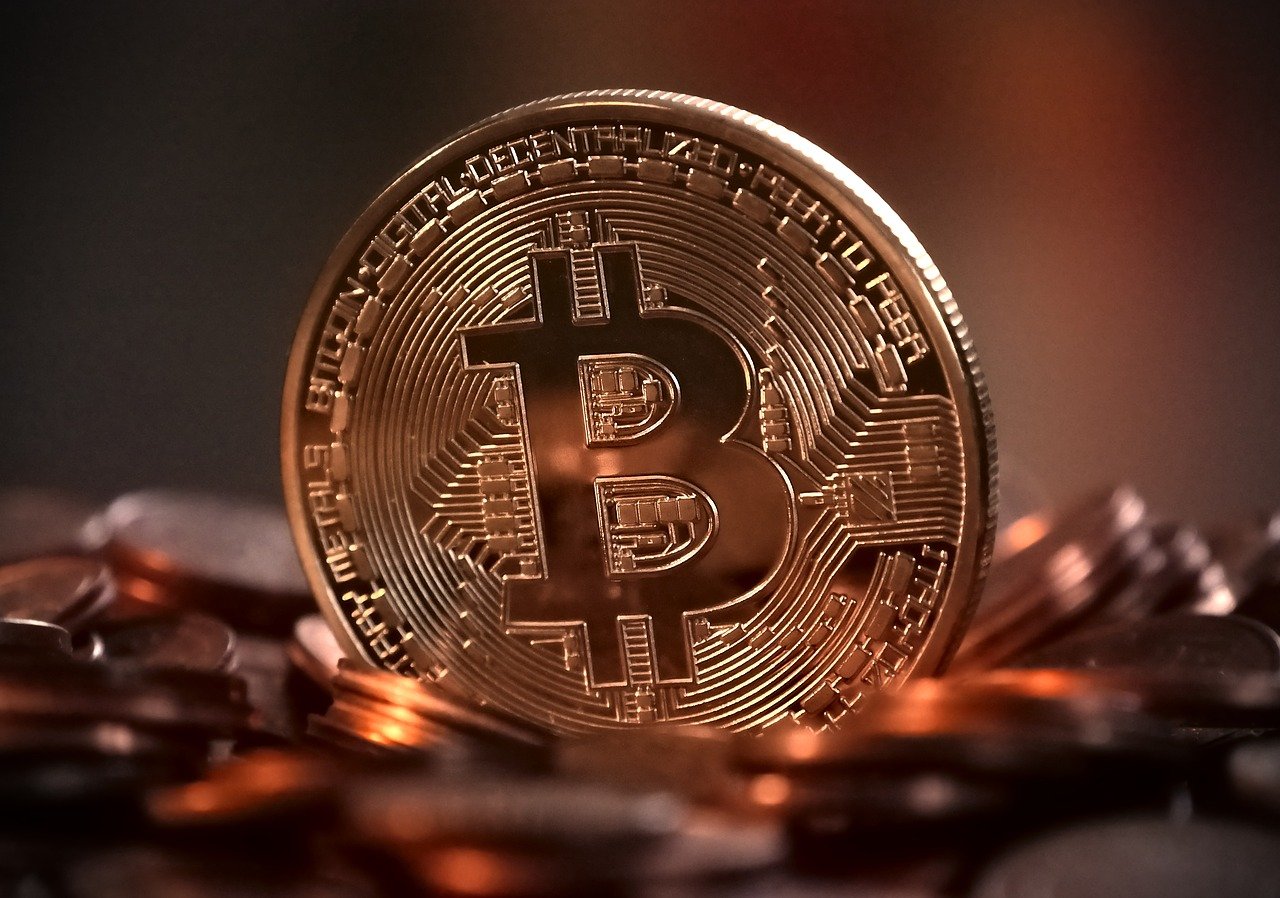 a bitcoin "coin" sitting amid a bunch of copper colored coins strewn in a hazy closeup image
